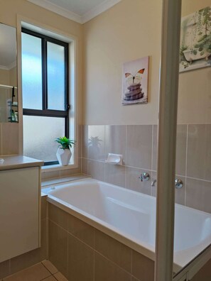 A modern bathroom with a bathtub, a window with frosted glass, a potted plant, and a wall-mounted artwork. - Beach&Winery retreat with Lux King, 2 Queen beds, 5BR2bath, sleeps12, Neflix (Christie Downs)