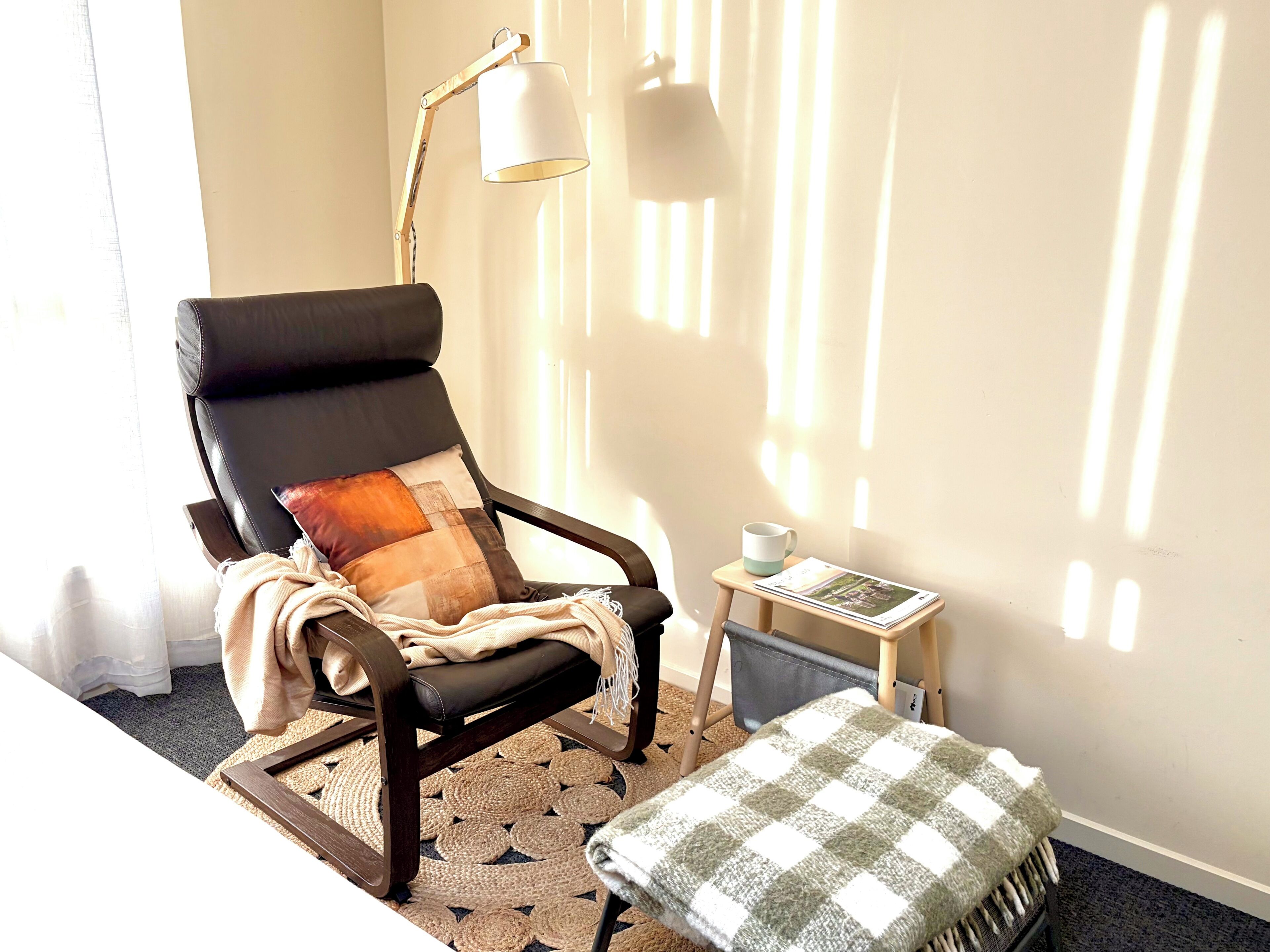 Een kamer met een zwarte lederen fauteuil, een houten vloer, een klein tafeltje met een kopje en een tijdschrift, en een lamp.