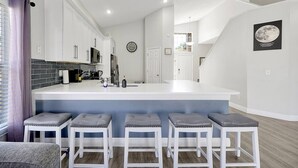 A modern kitchen with white cabinets, a central island with bar stools, and a clock on the wall. - Fully Renovated Disney Villa with Private Pool, King size Beds in Davenport (Davenport)