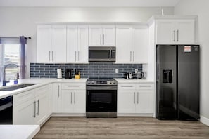 A modern kitchen with white cabinets, a stainless steel refrigerator, a microwave, a stove, and a coffee maker.