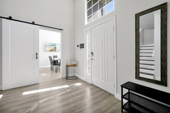 Un pasillo con una puerta corredera, un comedor con sillas y una mesa, y un espejo grande en la pared.