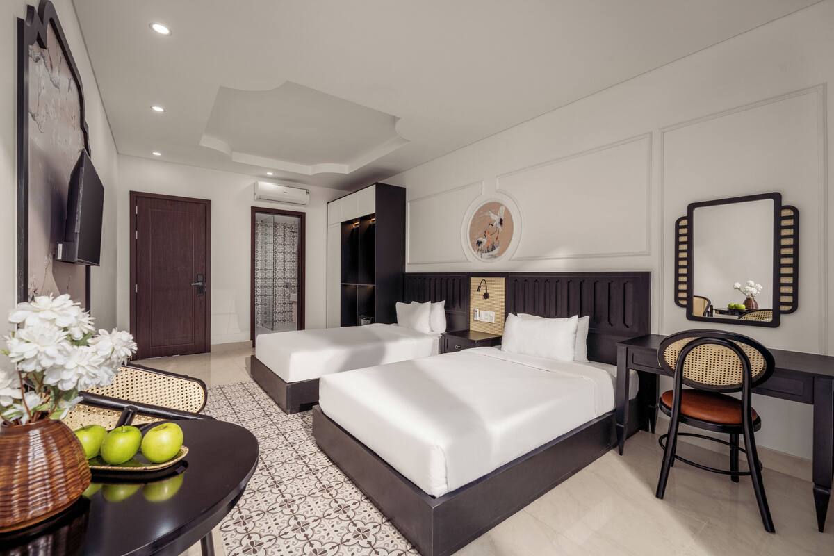 Habitación de hotel con dos camas, un escritorio, una silla, un televisor y un adorno en la pared.