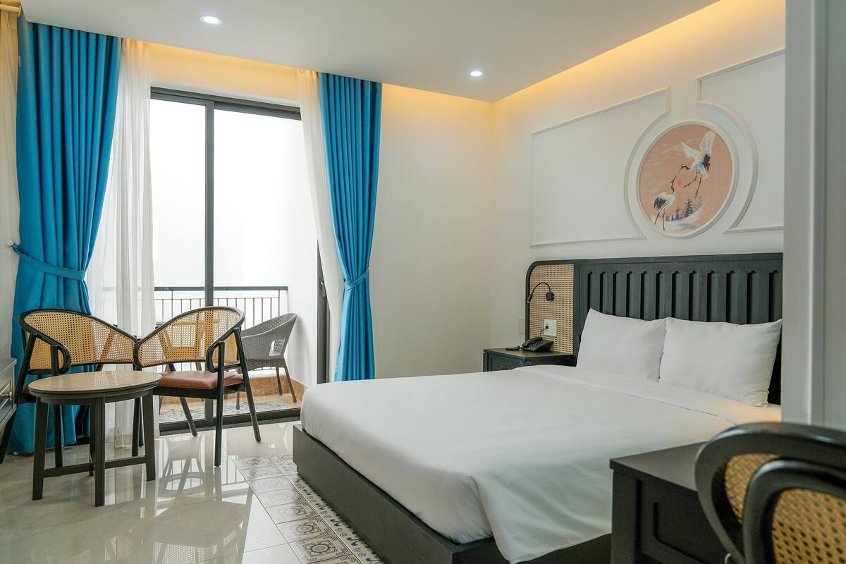 Una habitación de hotel con una cama grande, dos sillas, una mesita de noche y un cuadro en la pared.