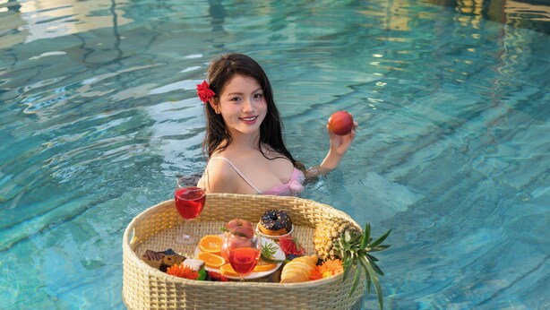 Une personne dans une piscine, tenant un panier rempli de fruits et une boisson.