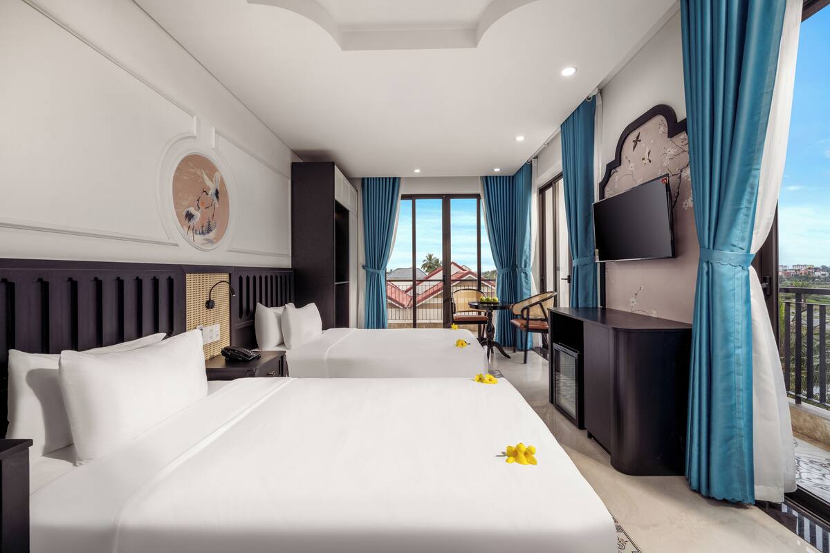 Habitación de hotel con dos camas, un escritorio, televisor y un balcón con vistas.