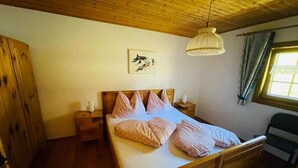 A wooden bed with a headboard, a bedside table, and a hanging light fixture in a room with wooden walls and a window with curtains. - Stallon apartment with balcony (Nostra)