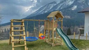 A wooden playground with a slide and swings, set against a mountainous backdrop. - Stallon apartment with balcony (Nostra)