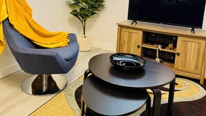 A living room with a blue chair, a small table, a TV, and a cabinet. - 2-bedroom apartment in wonderful SW Edmonton with WiFi, fitness equipment. (Edmonton)