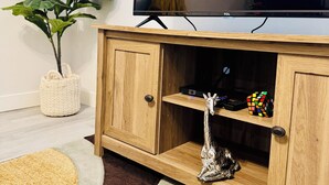 A living room with a flat-screen TV mounted on a wooden cabinet, a potted plant, a colorful rug, and a decorative giraffe figurine. - 2-bedroom apartment in wonderful SW Edmonton with WiFi, fitness equipment. (Edmonton)