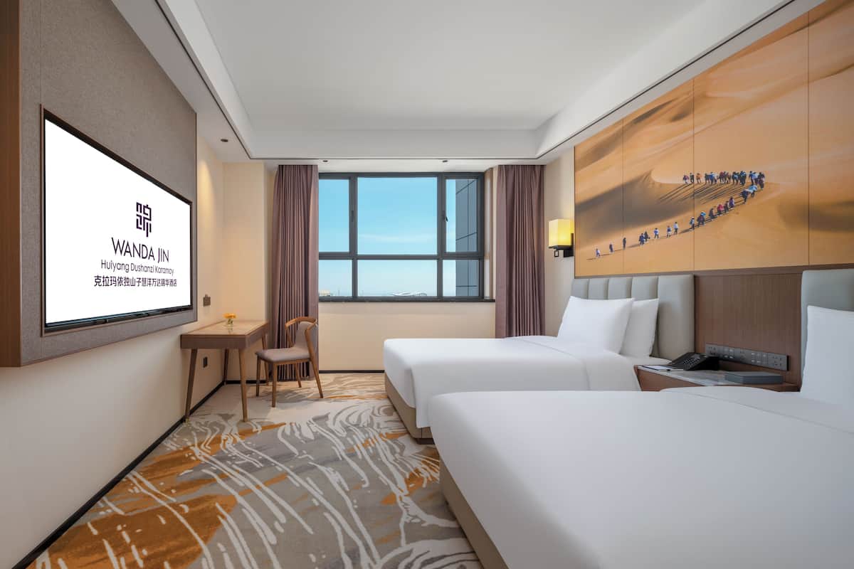 A hotel room with two beds, a large window, a wall-mounted TV, and a view of the sea.