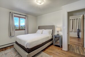 Relax in this serene bedroom with a large bed against a wall, a window with curtains, and a bedside table with a lamp.