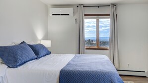 A bedroom with a bed, an air conditioning unit, a window with curtains, and a ceiling fan. - Sunset Ridge (Penrose)