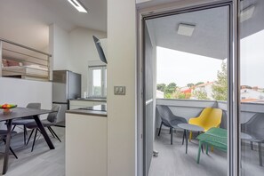 A modern kitchen with a dining area, a balcony with chairs, and a view of the city.