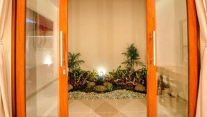 Une entrée moderne avec des portes en verre, un sol carrelé et un petit jardin de rocaille agrémenté de plantes.