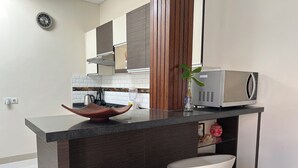 Une cuisine moderne avec un îlot central, des tabourets de bar blancs, un four à micro-ondes et une plante.
