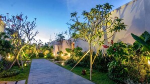 Un sentier de jardin avec une allée dallée, bordé de différentes plantes et arbres.