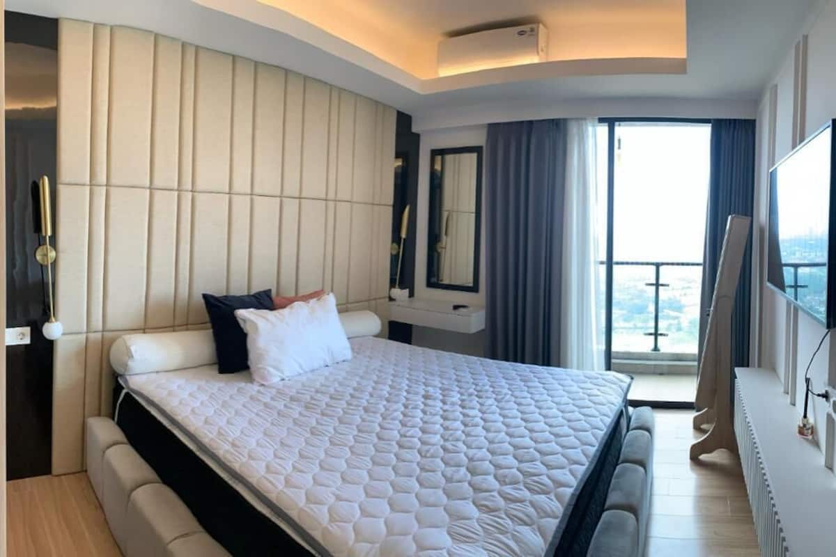 Une chambre d’hôtel moderne dotée d’un grand lit, d’une banquette intégrée, d’une coiffeuse avec miroir et d’un balcon offrant une vue agréable.