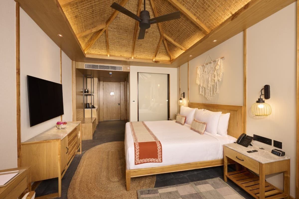 Ein modernes Hotelzimmer mit einem großen Bett, Holzmöbeln, einem Flachbildfernseher, einem Schreibtisch und einem Deckenventilator.
