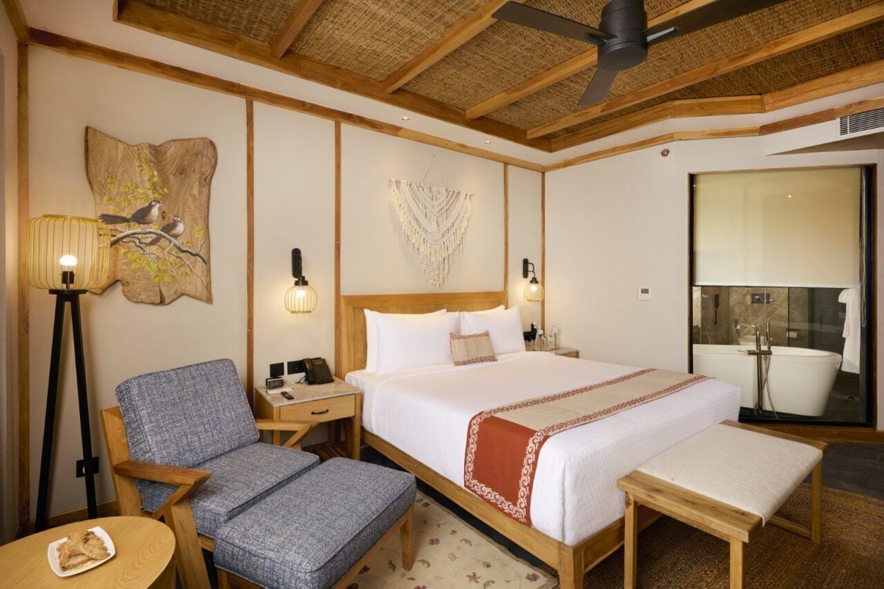 A hotel room with a large bed, a chair, a desk, a lamp, and a view of the bathroom.