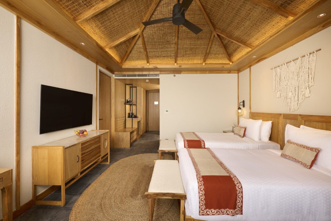 A hotel room with a large bed, a TV, wooden furniture, and a ceiling fan.