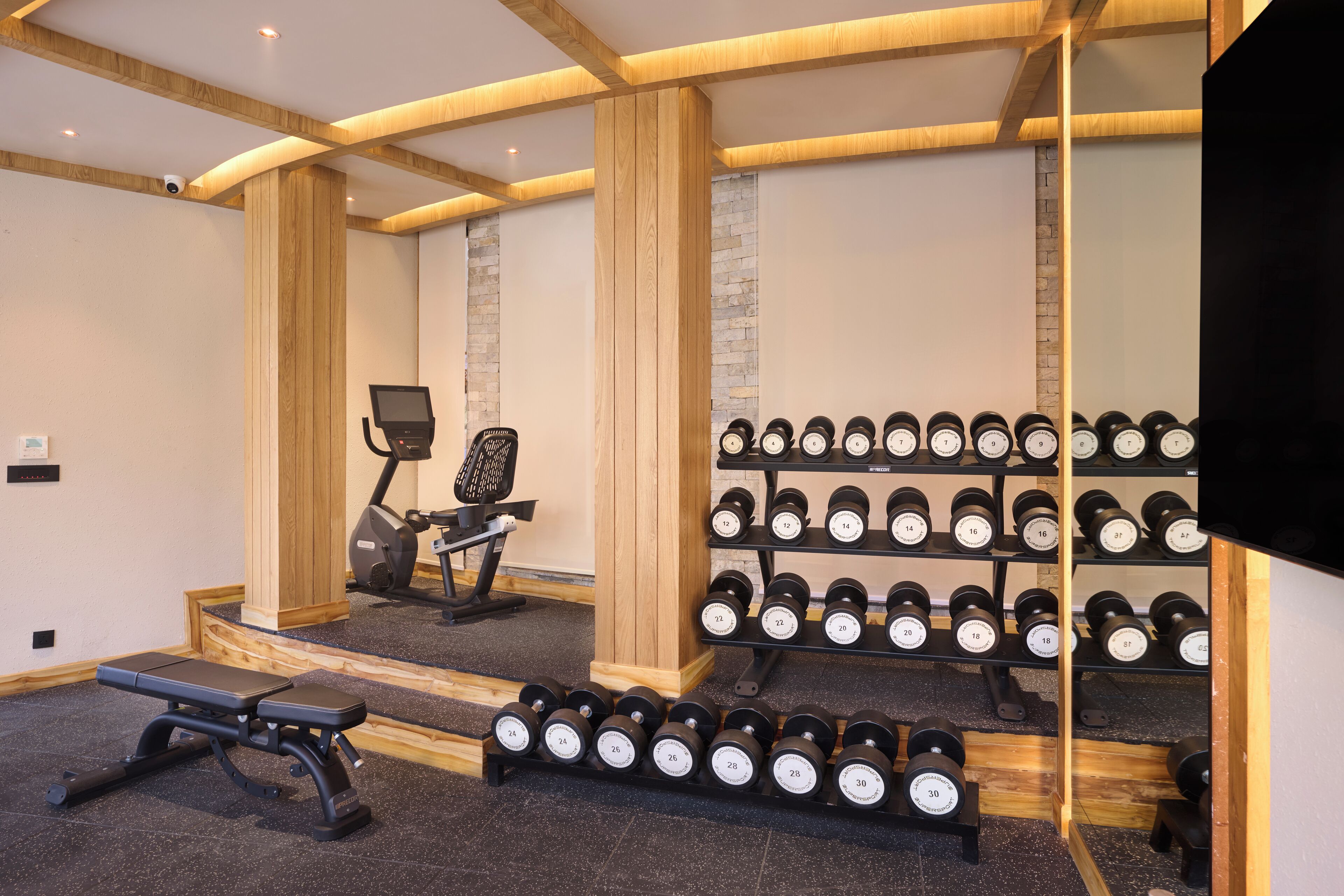 A gym with exercise equipment, a bench, and a wall-mounted rack of dumbbells.