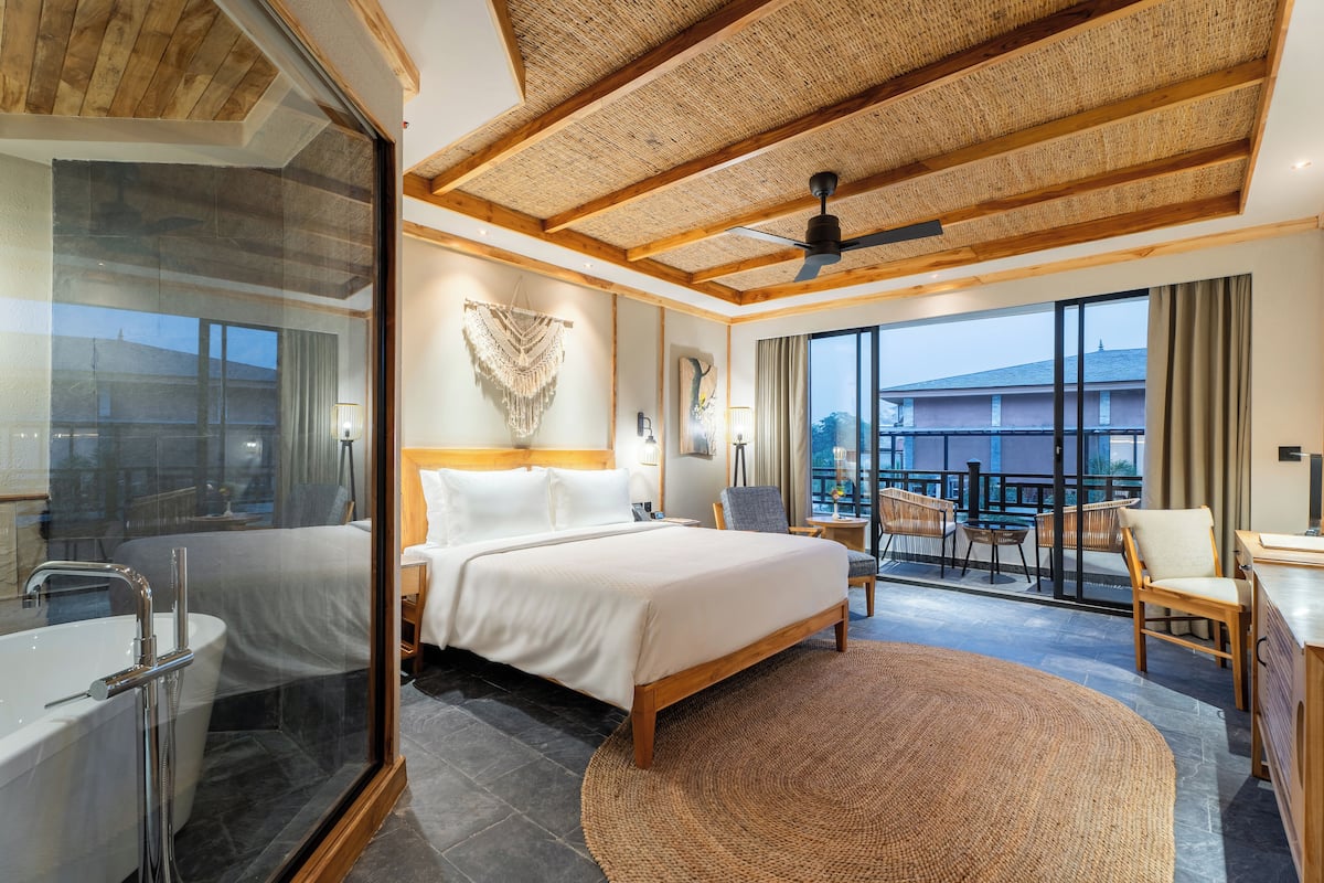Ein modernes Hotelzimmer mit einem großen Bett, einer Sitzecke mit Blick, einem Balkon und einem Badezimmer mit einer Badewanne.