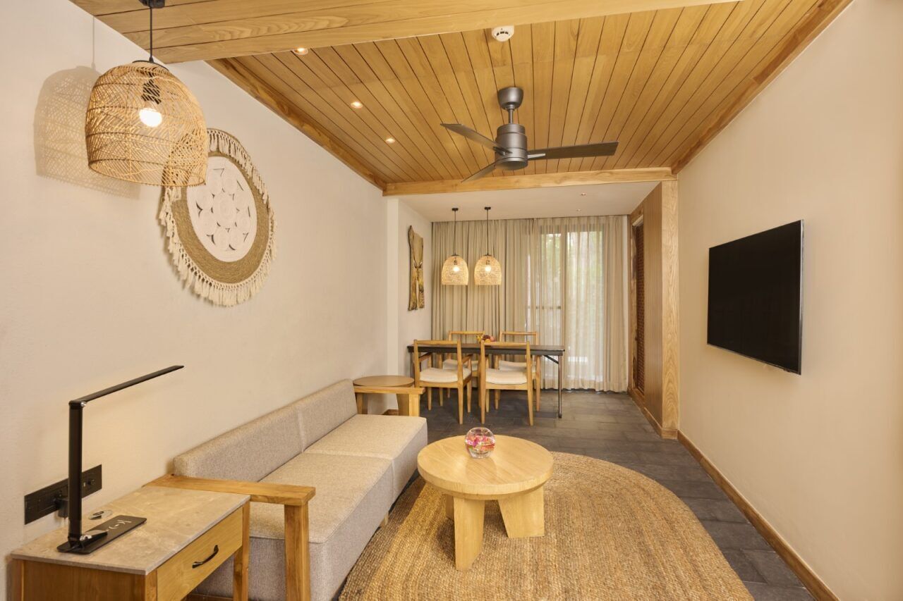 Una sala moderna con techo de madera, ventilador de techo, sofá, mesa de centro, televisor y un comedor con mesa y sillas.