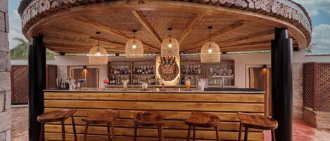 A bar area with wooden stools, a bar counter, and hanging pendant lights.