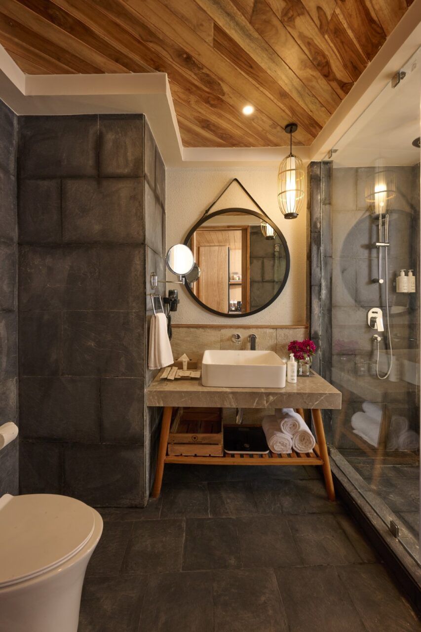 A modern bathroom with a wooden ceiling, a large mirror, a built-in sink, and a glass shower enclosure.