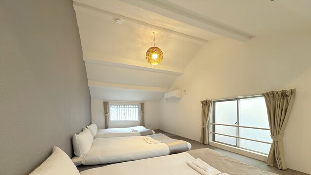 Une chambre d’hôtel avec deux lits, une grande fenêtre avec des rideaux, un luminaire au plafond et une petite fenêtre avec des stores.