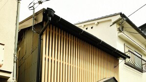Un bâtiment avec une porte noire, une petite fenêtre et une façade en bois à lattes.
