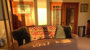 A cozy living room with a sofa, two green pillows, and a colorful quilt. - Auke Bay View Studio (Juneau)