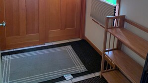 A room with a wooden door, a window with blinds, a wooden bench, and a mat at the entrance. - Auke Bay View Studio (Juneau)