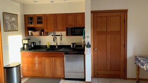A compact kitchen with wooden cabinets, a stainless steel dishwasher, a microwave, and a coffee maker. - Auke Bay View Studio (Juneau)