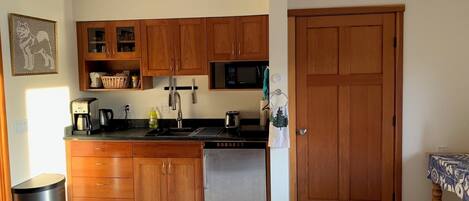 A compact kitchen with wooden cabinets, a stainless steel dishwasher, a microwave, and a coffee maker.