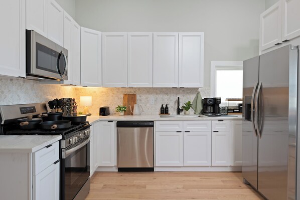 A modern kitchen with white cabinets, stainless steel appliances, and a wooden floor.