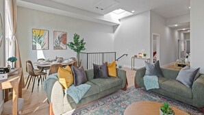 A modern living room with a sofa, coffee table, and dining area. - Cozy 3BR Stylish Home near Bus+PATH Access to NYC Metlife with Skylight Family (Jersey City)