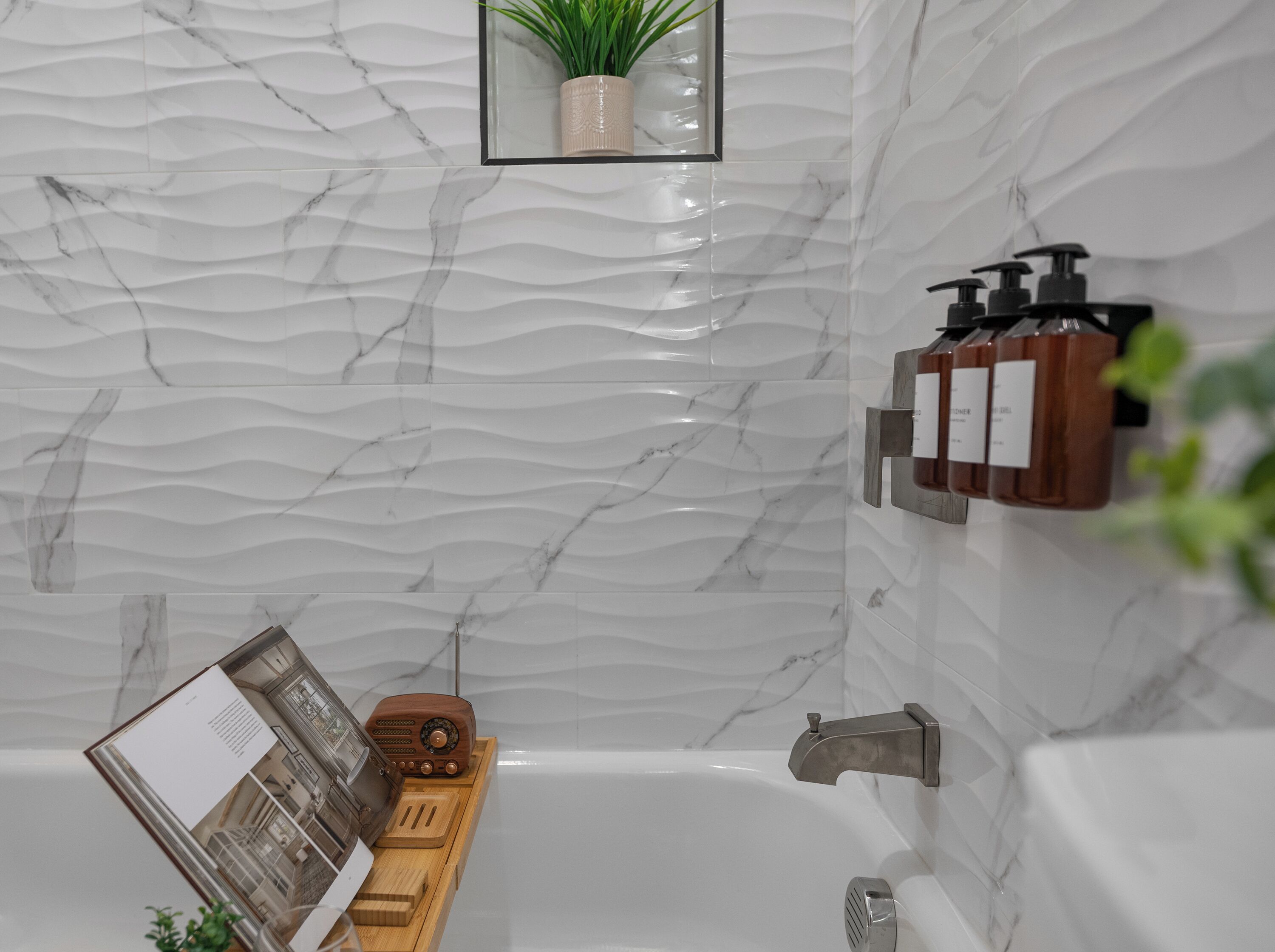 A bathroom with a marble wall, a wooden radio, a plant, and a shelf with bottles.