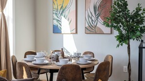 A dining area with a round table set for six, surrounded by six chairs. There are two framed artworks on the wall above the table. - Cozy 3BR Stylish Home near Bus+PATH Access to NYC Metlife with Skylight Family (Jersey City)