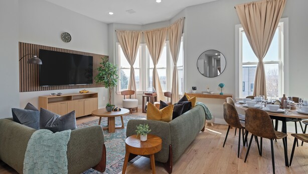 A modern living room with a sofa, a dining table, and a TV. - Cozy 3BR Stylish Home near Bus+PATH Access to NYC Metlife with Skylight Family (Jersey City)