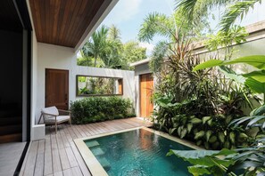 A modern outdoor pool area with wooden decking, a white chair, and lush tropical plants. - Umayam Sanctuary by Alfred in Bali (Canggu)