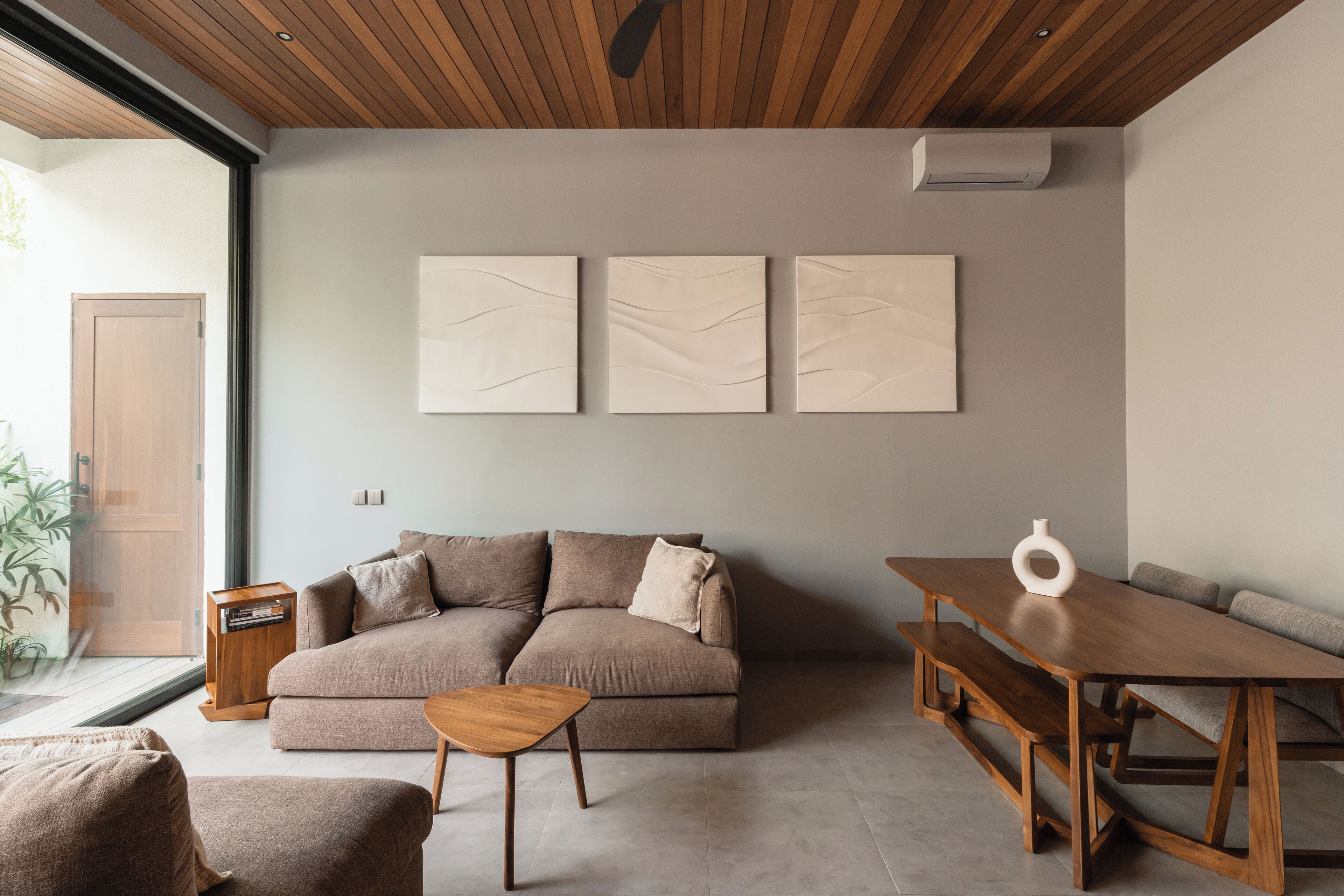 Un soggiorno moderno con un divano componibile, un tavolino in legno e un tavolo da pranzo con panche. Sopra il divano, tre opere d'arte astratte alle pareti.
