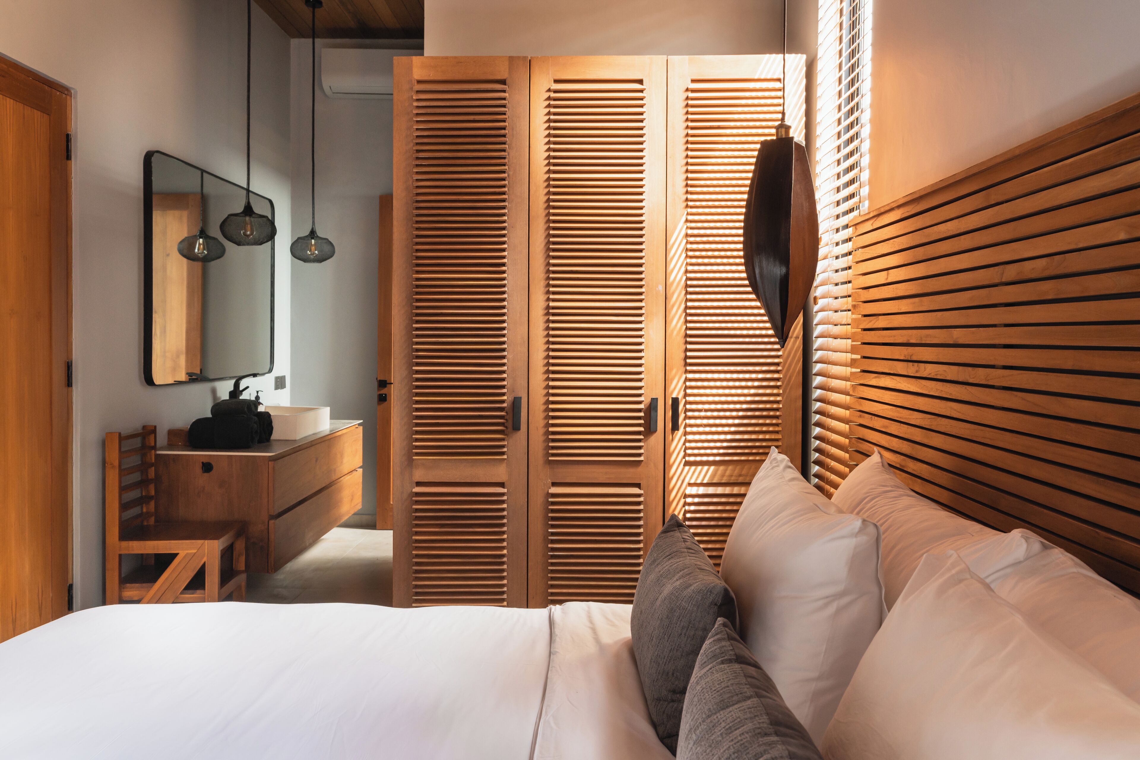 A bedroom with a wooden headboard, a bed with white bedding, a wooden dresser, a mirror, and a wooden wardrobe.
