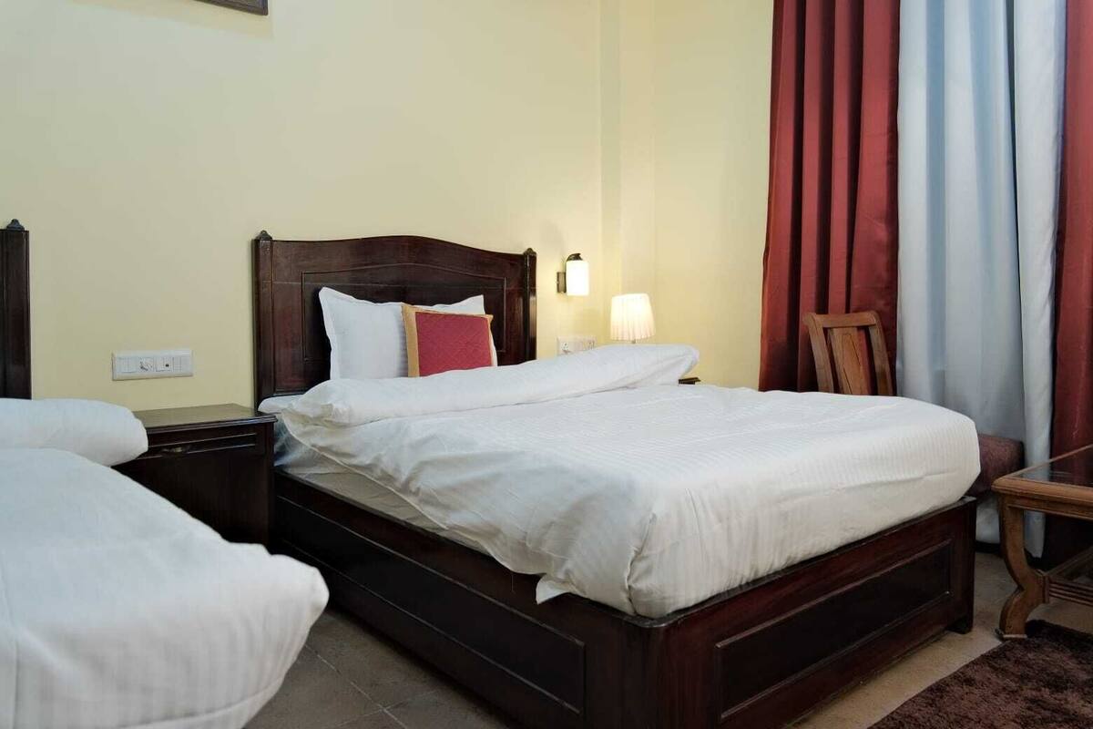 Una habitación de hotel con una cama de madera, una mesita de noche, una lámpara y una silla.