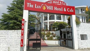Der Eingang zum Luv Hill Hotel & Cafe mit einem roten Schild, einem schwarzen Tor und einem weißen Gebäude mit Balkonen.