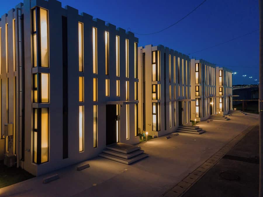 A modern building with a symmetrical facade, featuring evenly spaced vertical windows and a central entrance with steps leading up to it.