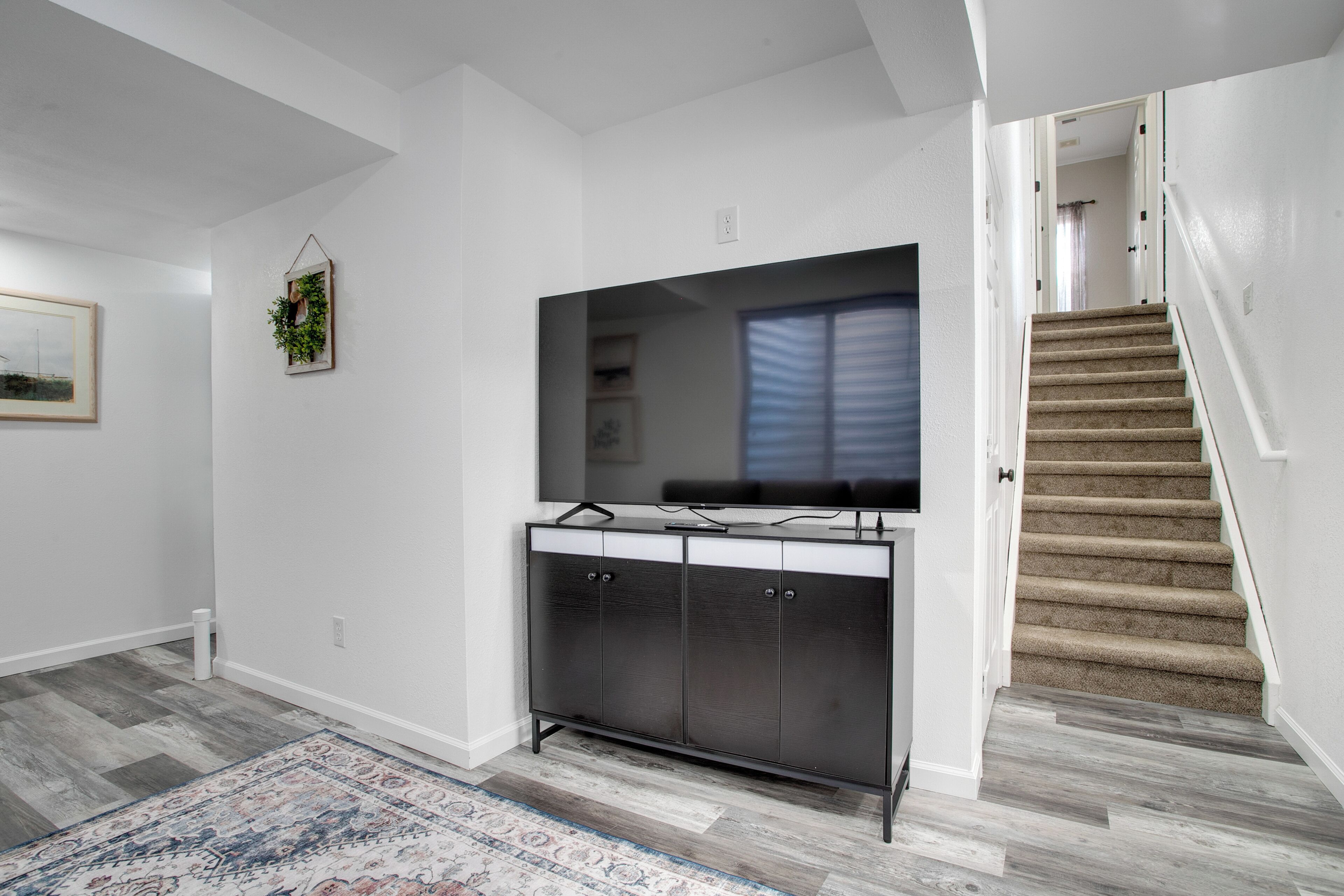 Un apartamento moderno con un espejo grande, televisión empotrada, una escalera y una alfombra estampada.