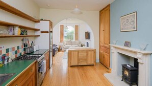 A kitchen with wooden cabinets, a stove, and a dining area with a sofa and table. - Colourful Victorian Home in Redland with Garden (Bristol City)