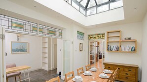 A spacious dining area with a high ceiling and skylight, a wooden dining table set for six, and a bookshelf with books. - Colourful Victorian Home in Redland with Garden (Bristol City)