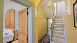 A hallway with a wooden door, a white sofa, and a staircase with a patterned rug. - Colourful Victorian Home in Redland with Garden (Bristol City)